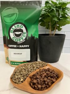 Photo showing close up of green and roasted decaf with a bag of BCR Decaf and small coffee tree.