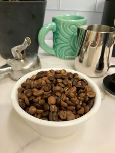 Photo showing close up of dark and medium roasted coffee beans blended together for BCR Espresso in a bowl with coffee gear in the background.