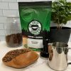 Photo showing bag of ER's Favorite with bowl of roasted beans, milk pitcher, tamper, coffee canister, and small coffee tree.